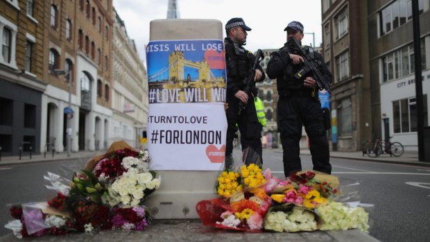 Armed police stand guard in front of floral tributes on Southwark Street near the scene of the terrorist attack.