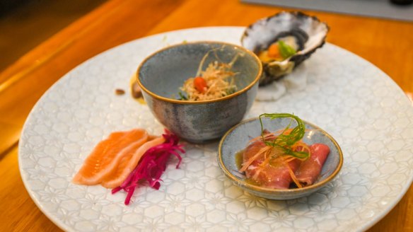 Appetiser plate with raw and cooked slices of wagyu, an oyster with ponzu, lightly cured salmon and a small dish of spinach.