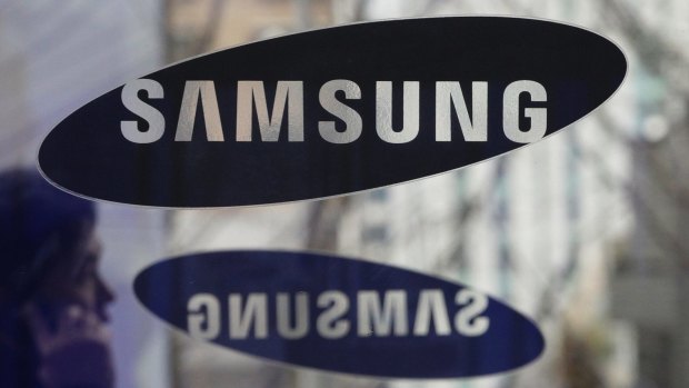 A man with a mobile phone walks by the Samsung Electronics logos at its headquarters in Seoul, South Korea. 