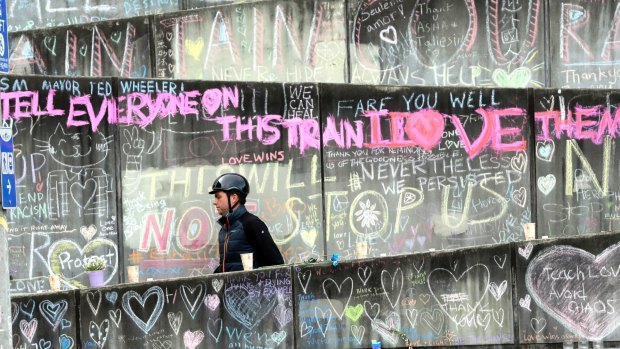 A cyclist is surrounded by messages in support of the two men fatally stabbed on a train in Portland on May 26. In pink are the reported last words of Taliesin Namkai-Meche.