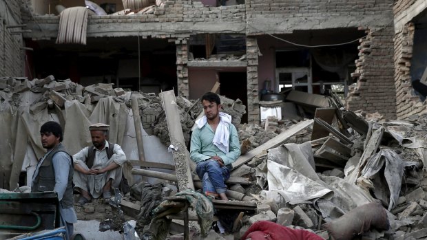 Men sit amid debris at the site a truck bomb blast in Kabul, on August 7, 2015. 