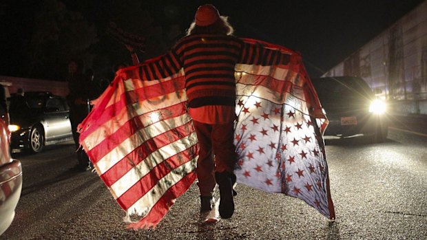 Querying justice system: A protester carrying an upside-down flag marches past cars on a highway in Oakland, California.