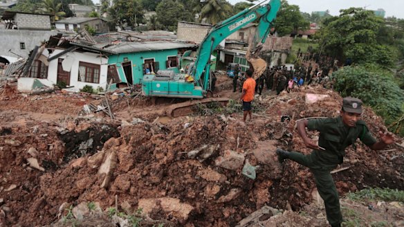 Sri Lankan army soldiers and rescue workers stand near buried houses.