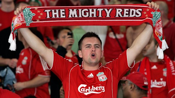 A Liverpool football fan holds up a scarf in the stands during a match.