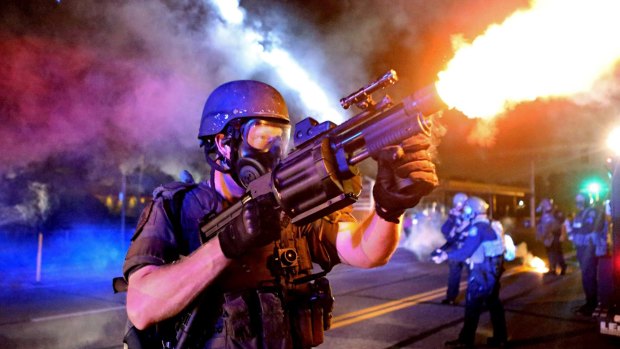 St Louis County Police tactical team fires tear gas into a crowd of people in Ferguson.