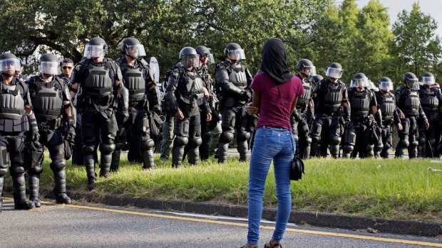 A protester watches as police in riot gear clear the street of protesters in front of the Baton Rouge Police Department headquarters.