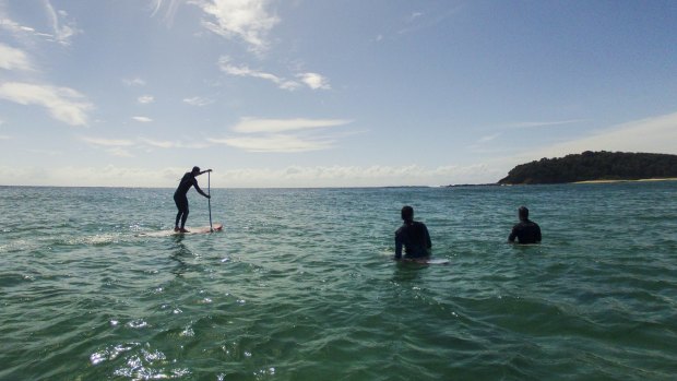 Stand up paddle boarders and surfers at Lake Tabourie on the South Coast of NSW.