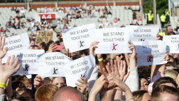 People in the One Love Manchester concert crowd hold placards reading "We Stand Together".