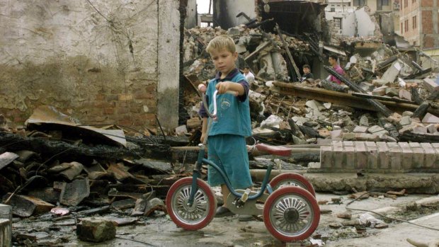 A young Kosovo ethnic Albanian boy moves his bike through the ruins of the streets in Peja, Kosovo, in 1999.