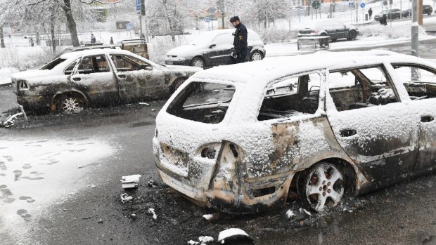 A police man investigate a burned out car in the suburb Rinkeby outside Stockholm.