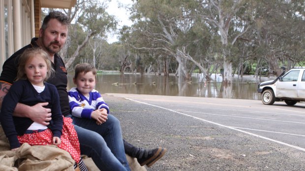 Glenelg Inn publican Troy Robbins and his children Marlee and Nate sit on sandbags outside the hotel at Casterton. 