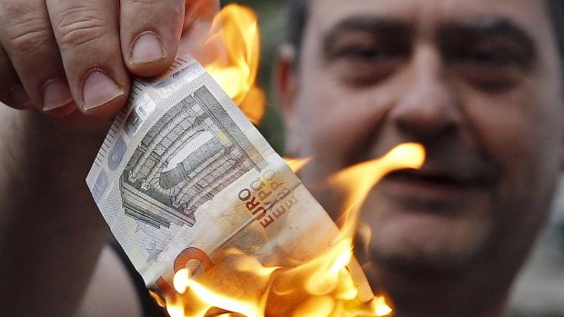 An anti-austerity protester burns a euro note during a demonstration outside the European Union offices in Athens, Greece.