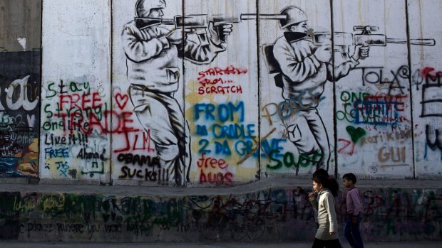 Children walk past graffiti on the Palestinian side of the separation wall in the West Bank.