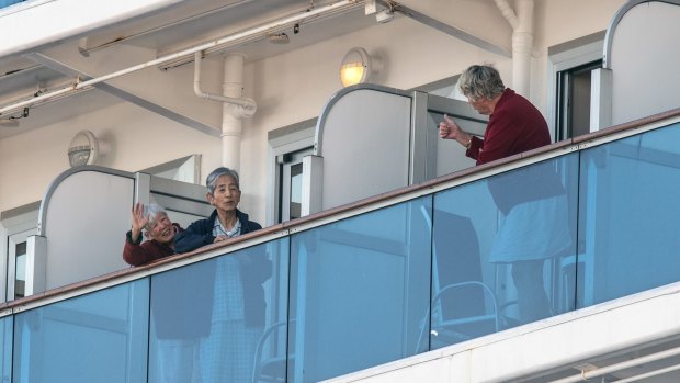 A woman gives a thumbs up to fellow passengers as they stand on their cabin balconies while waiting onboard the Diamond Princess.