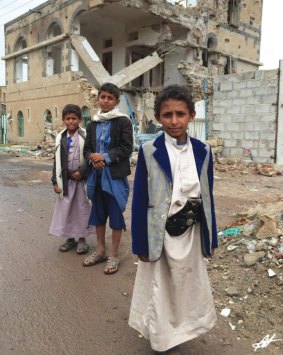 Boys from Yemen in their traditional dress stand in front of their bombed house.