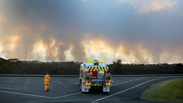A Rural Fire Service volunteer stands beside his tanker on the M1 motorway watching a bushfire on Maddens Plain on the Illawarra Escarpment. 