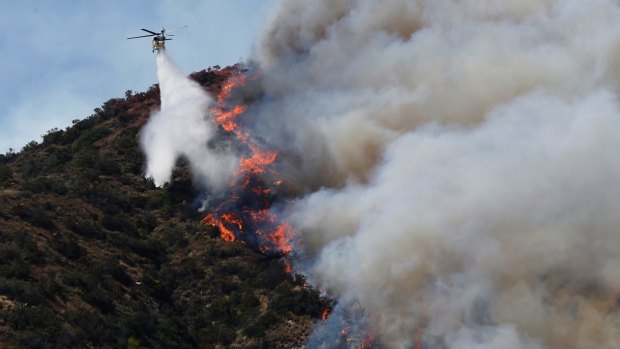 A helicopter drops water on wildfire on a hill near Azusa, California.