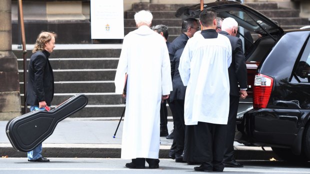 Angus Young carries a guitar as he watches brother Malcolm's casket carried to a hearse outside St Mary's Cathedral on Tuesday.