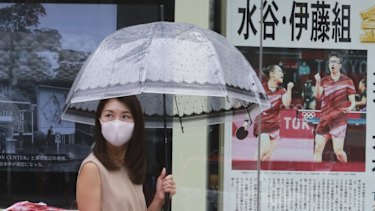 People wearing face masks to protect against the spread of the coronavirus walk past extra papers reporting on Japanese gold medallists at the Tokyo Olympics. 