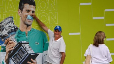 A spectator places a mask over the face of Novak Djokovic on a billboard at Melbourne Park.