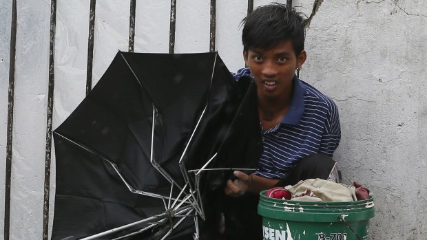 A boy holding a broken umbrella seeks shelter from the winds and rain in Manila.