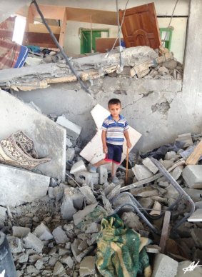 A boy in occupied Palestine stands in what remains of his bedroom after an air strike.