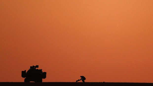 A Turkish soldier places a carpet next to a military vehicle as he watches fighting between Kurdish fighters and Islamic State militants.