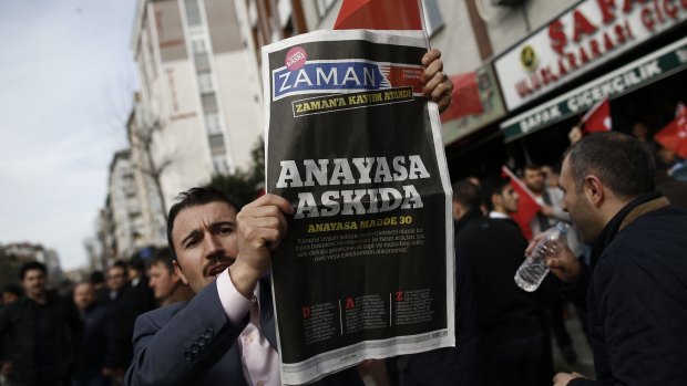 A man holds Saturday's copy of the newspaper which reads "the constitution suspended" as people gathered in support in Istanbul.
