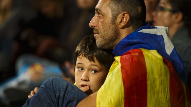 A man and his child listen to a televised speech by Spain's Prime Minister Mariano Rajoy after a banned Catalan referendum in Barcelona.