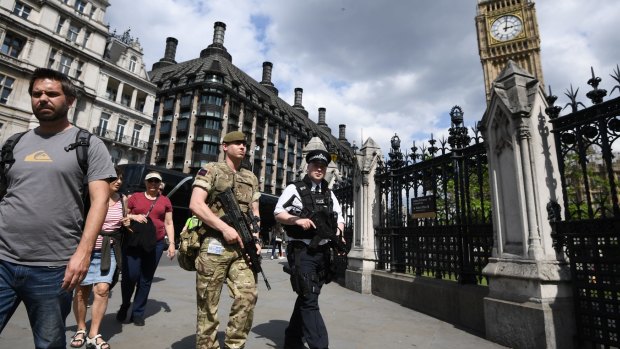 An armed soldier and an armed police officer patrol outside the Houses of Parliament.