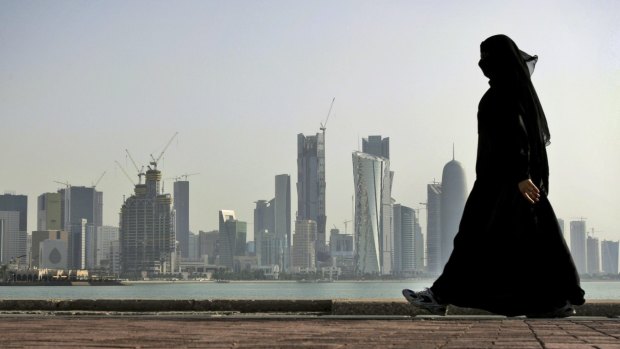 A Qatari woman walks in front of the city skyline in Doha, Qatar.