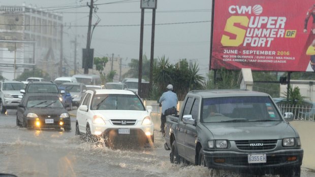 Cars drive along a street under heavy rain in downtown Kingston, Jamaica.