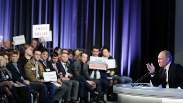 Russian President Vladimir Putin gestures as journalists show their posters with questions to him during his annual news conference in Moscow, Russia, on Friday