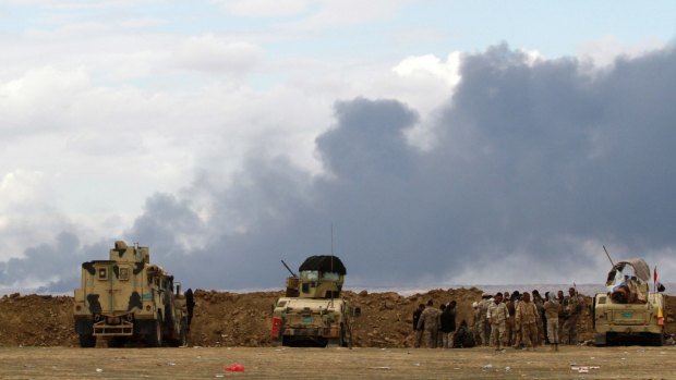 Iraqi soldiers gather near their vehicles as smoke rises from oil wells in the Ajil field, east of the city of Tikrit.
