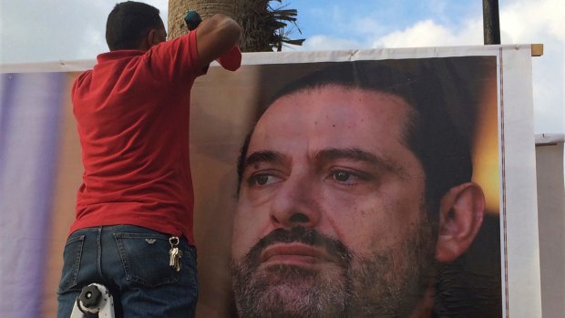 Workers hang a poster of outgoing Prime Minister Saad Hariri with Arabic words that read, "We are all Saad," on a seaside street in Beirut, Lebanon, on Thursday.