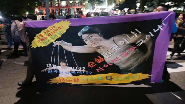 South Korean protesters carry a banner depicting South Korean President Park Geun-hye, left bottom, as a marionette and Choi Soon-sil.