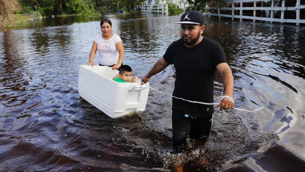 Alfonso Jose pulls his son, 2,in a cooler with his wife as they wade through floods in Florida.