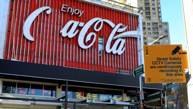 The iconic Coca-Cola sign, undergoing an update, stands amid the watchful eye of CCTV.