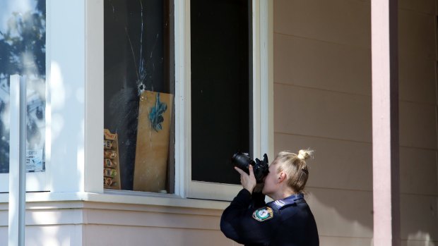 A police officer photographs the bullethole in the window of the home. 