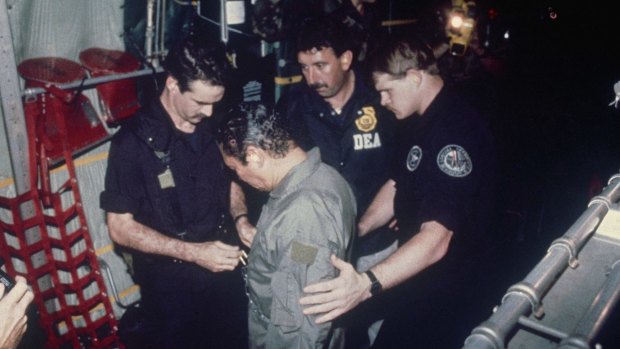 January 1990: Manuel Noriega watches as US Drug Enforcement Agents place chains around his waist aboard a C-130 transport plane.  