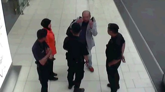 Kim Jong-nam, in grey, gestures towards his face while talking to airport security shortly before his death.