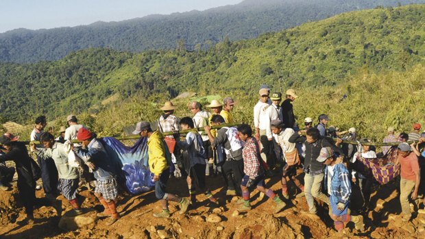 Jade mine workers and rescue members carrying victims of a landslide walk on dump soil in Hpakant, Kachin State, Myanmar on Sunday.