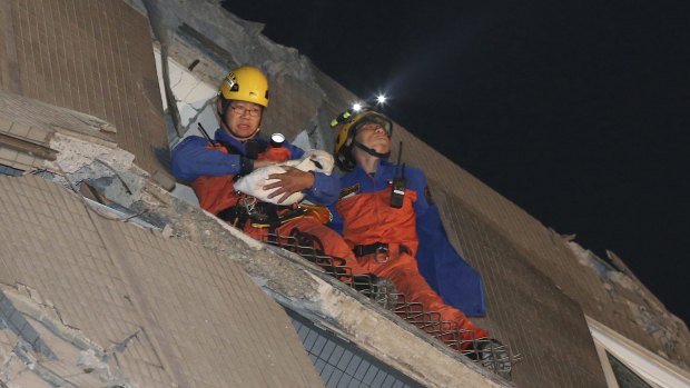 Rescue workers carry a baby swaddled in a cloth from the rubble of a toppled building.