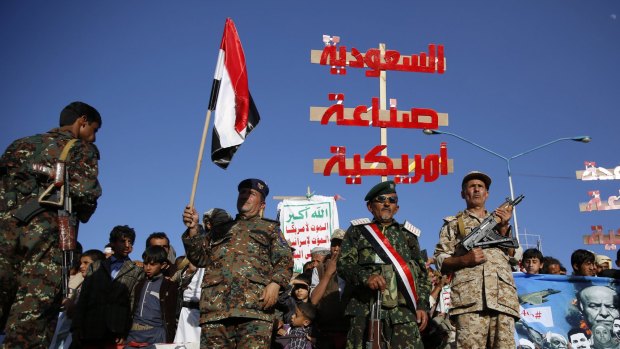 Houthi fighters hold a red banner that reads "Saudi Arabia is American made".  