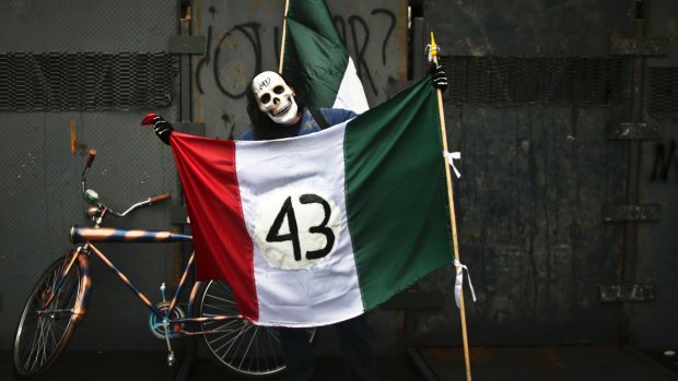 September 2015: A protester wearing a skull mask and holding a Mexican flag with its emblem covered with the number 43 stands in front of a police barrier during a march marking the first anniversary of the disappearance of 43 rural college students.