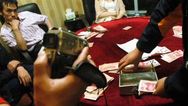 A Chinese man, left,  arrested for illegal gambling when police raided an illegal casino,  watches as money are confiscated in Chengdu, southwest China's Sichuan province, Tuesday, April 11, 2006. Chinese authorities are keen to crack down on illegal vices such as gambling and prostitution to counter critics who says the free wheeling capitalism introduced is also bringing in these unhealthy activities. (AP Photo/Color China Photo) ** CHINA OUT **
