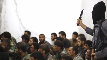 Ruthless ... A fighter from the Islamic State group, armed with a knife and an automatic weapon, stands over captured Syrian army soldiers and officers in August last year.