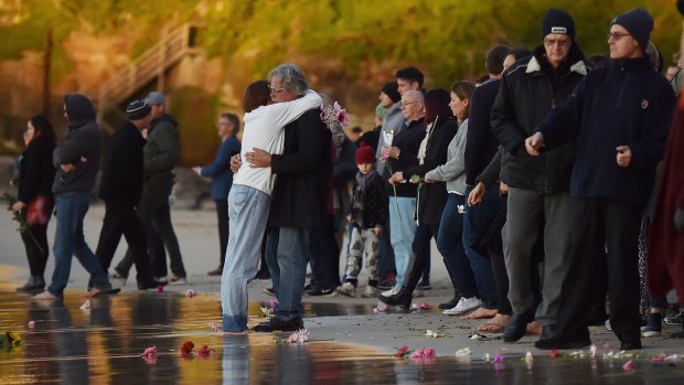 Parents of Justine Damond, Maryan Heffernan (centre left, white top, jeans) and John Ruszczyk (centre right, black coat, glasses) embrace at the Freshwater Beach water's edge during a vigil for their daughter. 
