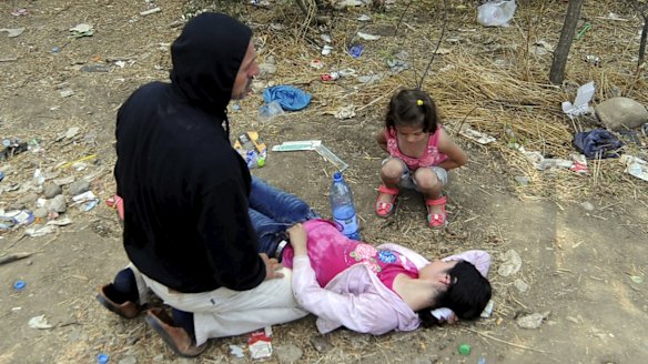 A man kneels next to his collapsed wife at the border.