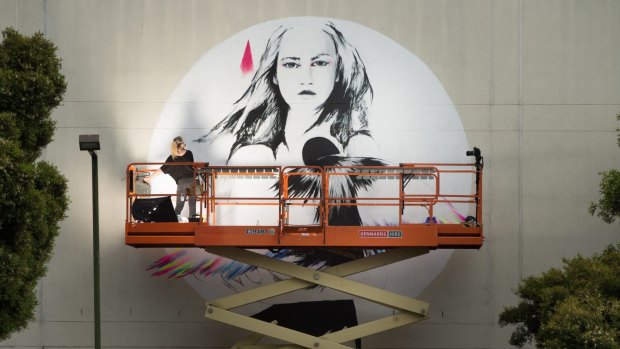 Street artist Vexta paints her image at the back of the St Kilda police station.
